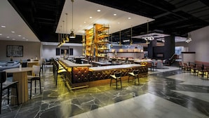 A modern bar area with a central bar, seating, and a staircase leading to an upper level. - Buffalo Marriott Niagara (Buffalo)