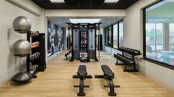 Uma academia com equipamentos de ginástica, bancos e um suporte na parede para halteres.