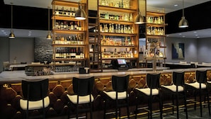 A bar area with multiple shelves of bottles, a bar counter, and several bar stools. - Buffalo Marriott Niagara (Buffalo)
