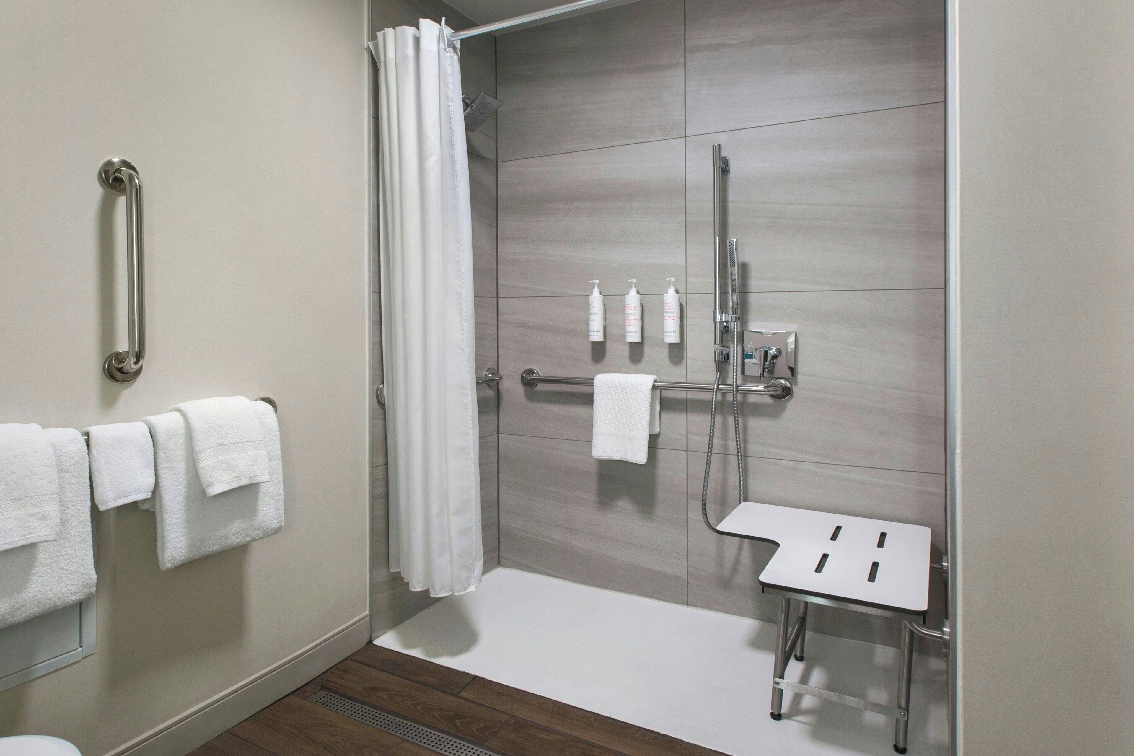 A modern bathroom with a shower, a handrail, a small table, and a towel rack.