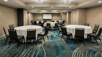 A conference room with round tables, chairs, a projector screen, and a carpeted floor.