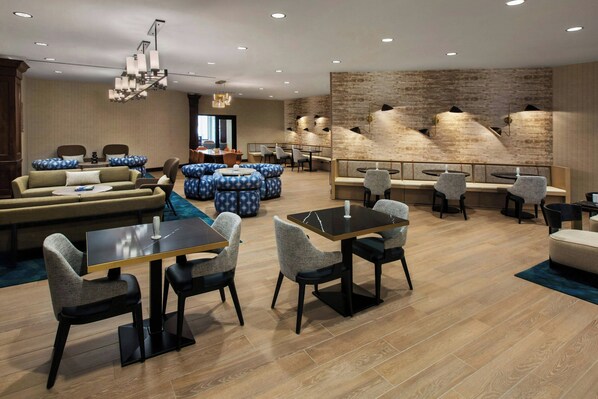 A modern hotel lobby with a mix of seating areas, including a sofa set, round tables, and chairs. - Buffalo Marriott Niagara (Buffalo)
