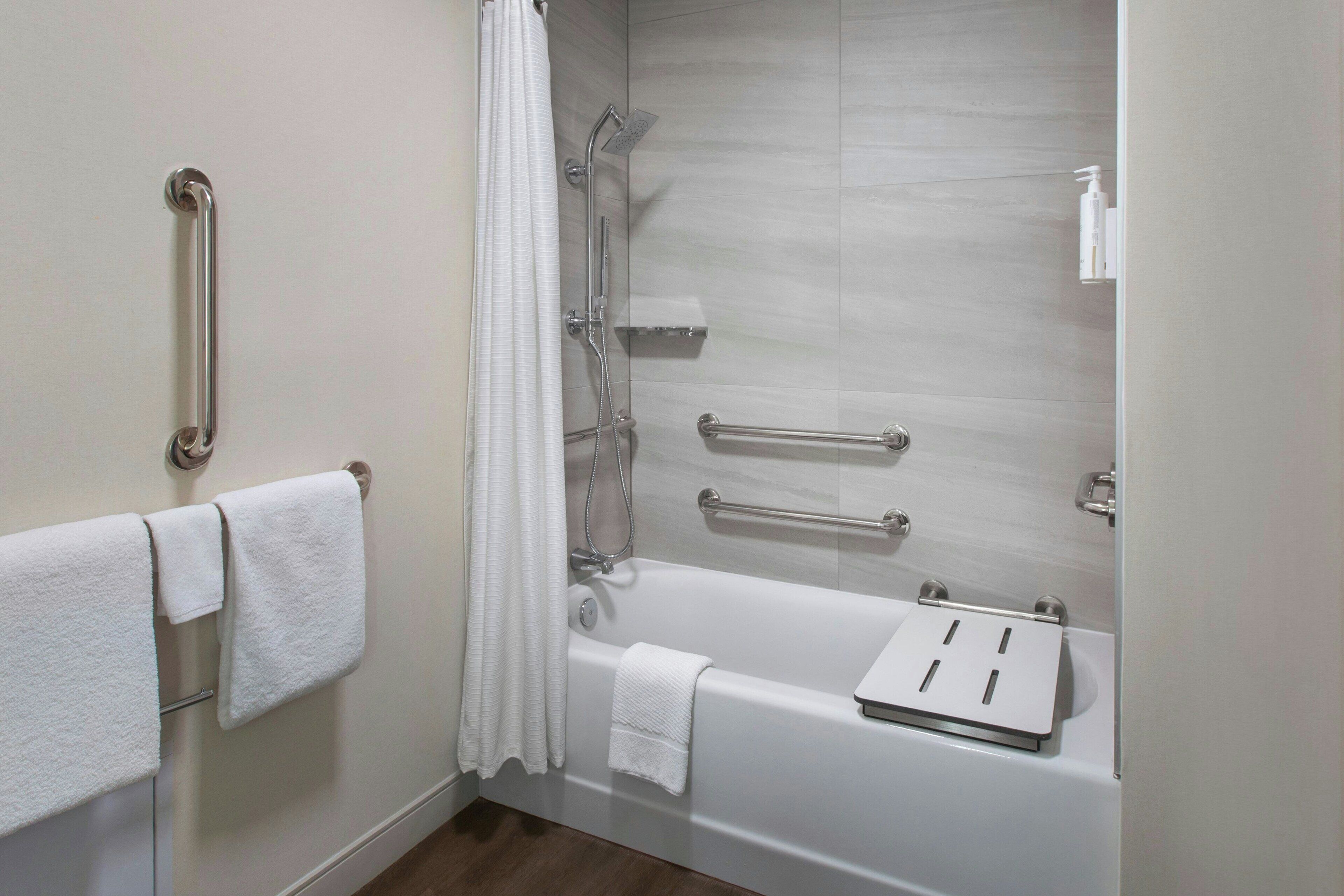 A bathroom with a bathtub, grab bars, a shower, and a towel rack.