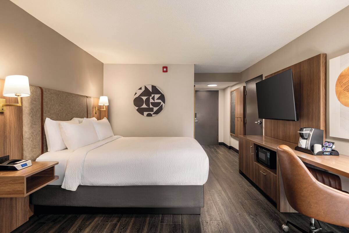 Quarto de hotel com cama, mesas de cabeceira, televisão, máquina de café e micro-ondas.