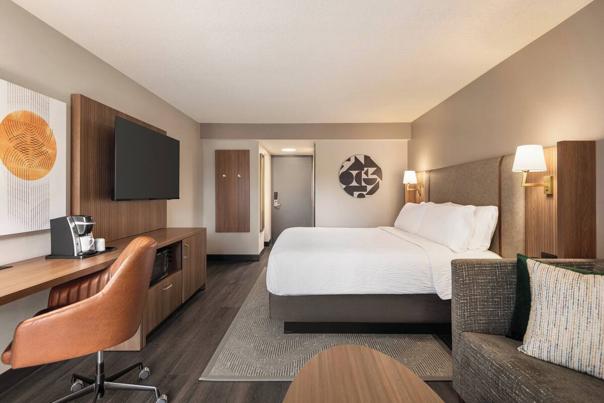 Quarto de hotel com cama, escrivaninha, cadeira, televisão e máquina de café.