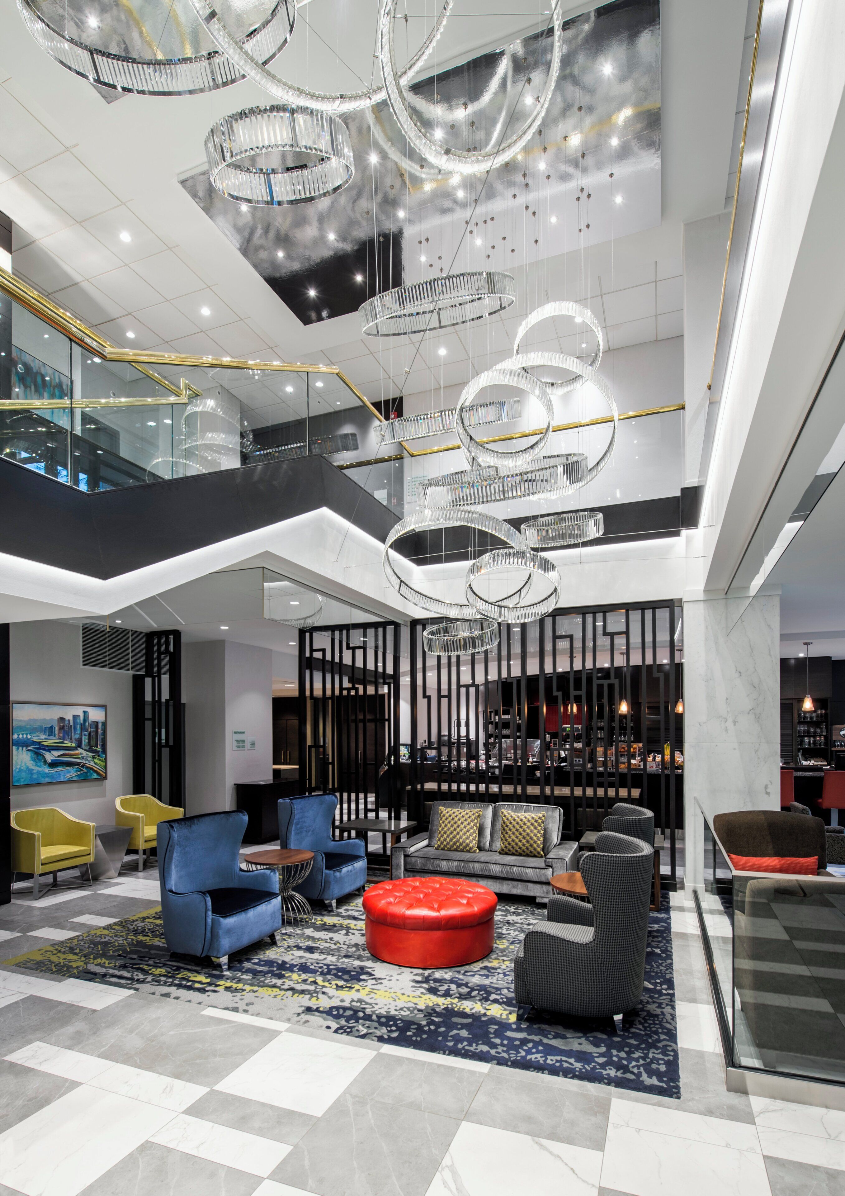 A spacious lobby with a high ceiling, modern chandeliers, and a seating area with sofas and ottomans.