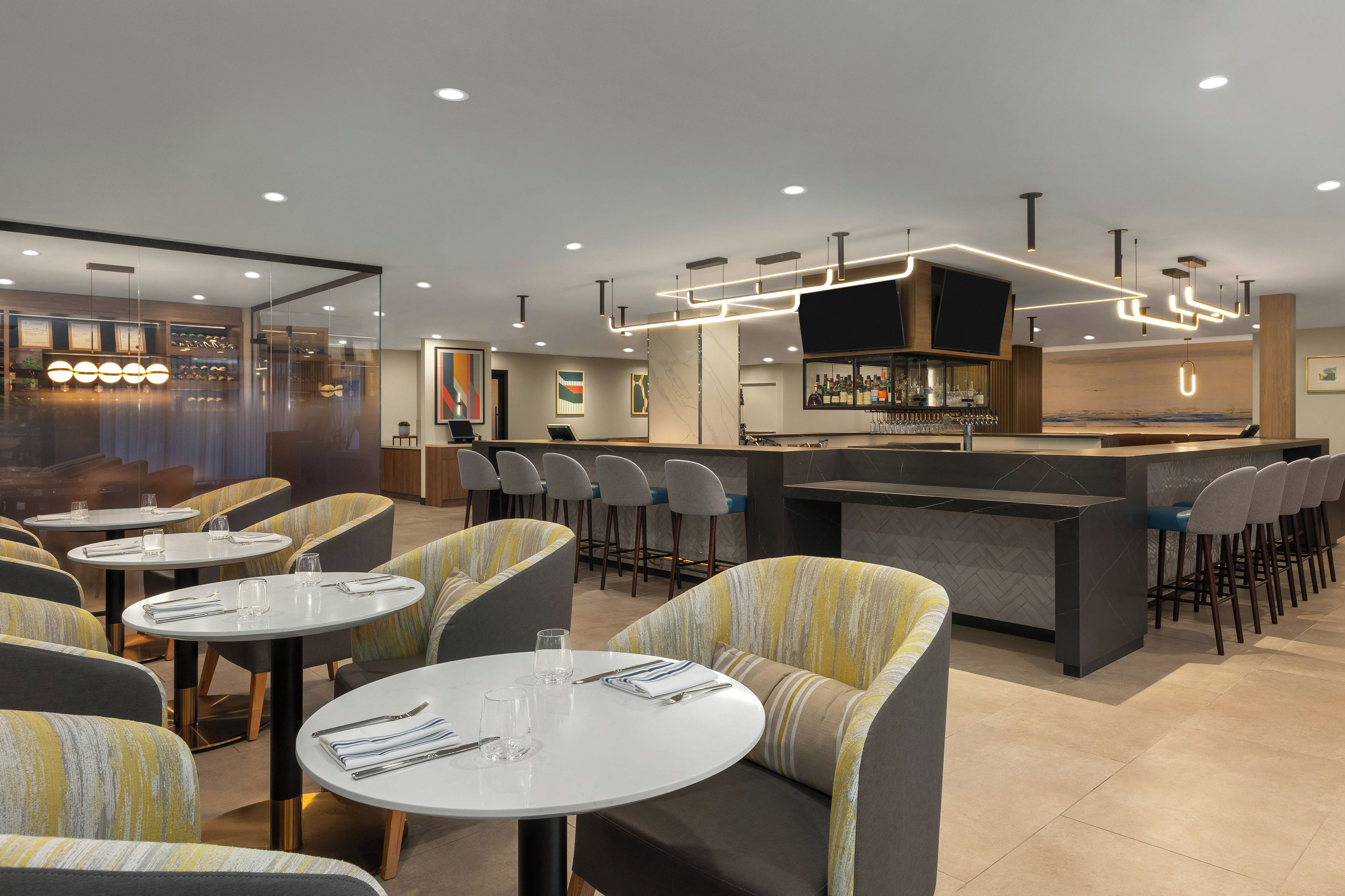 Un interior de restaurante moderno con mesas redondas, asientos de bar e iluminación contemporánea.