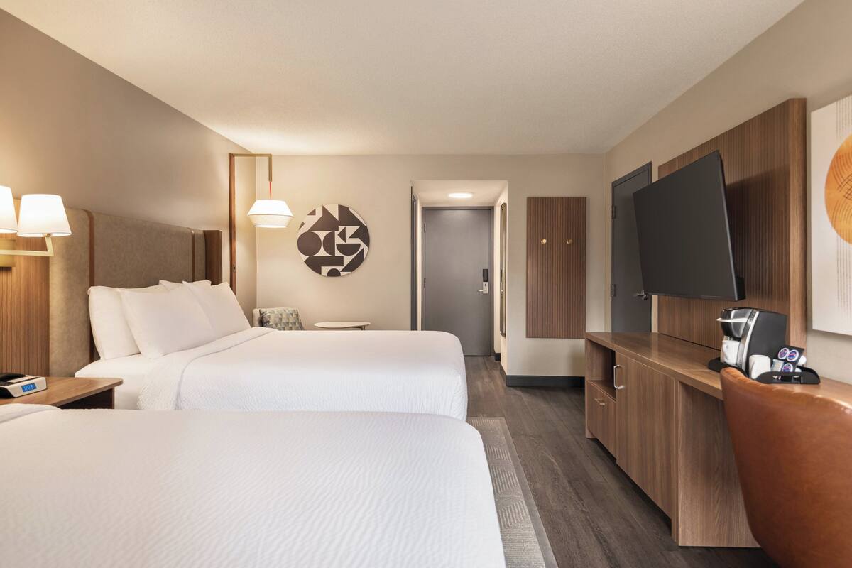Quarto de hotel com duas camas, televisão, escrivaninha e espelho.