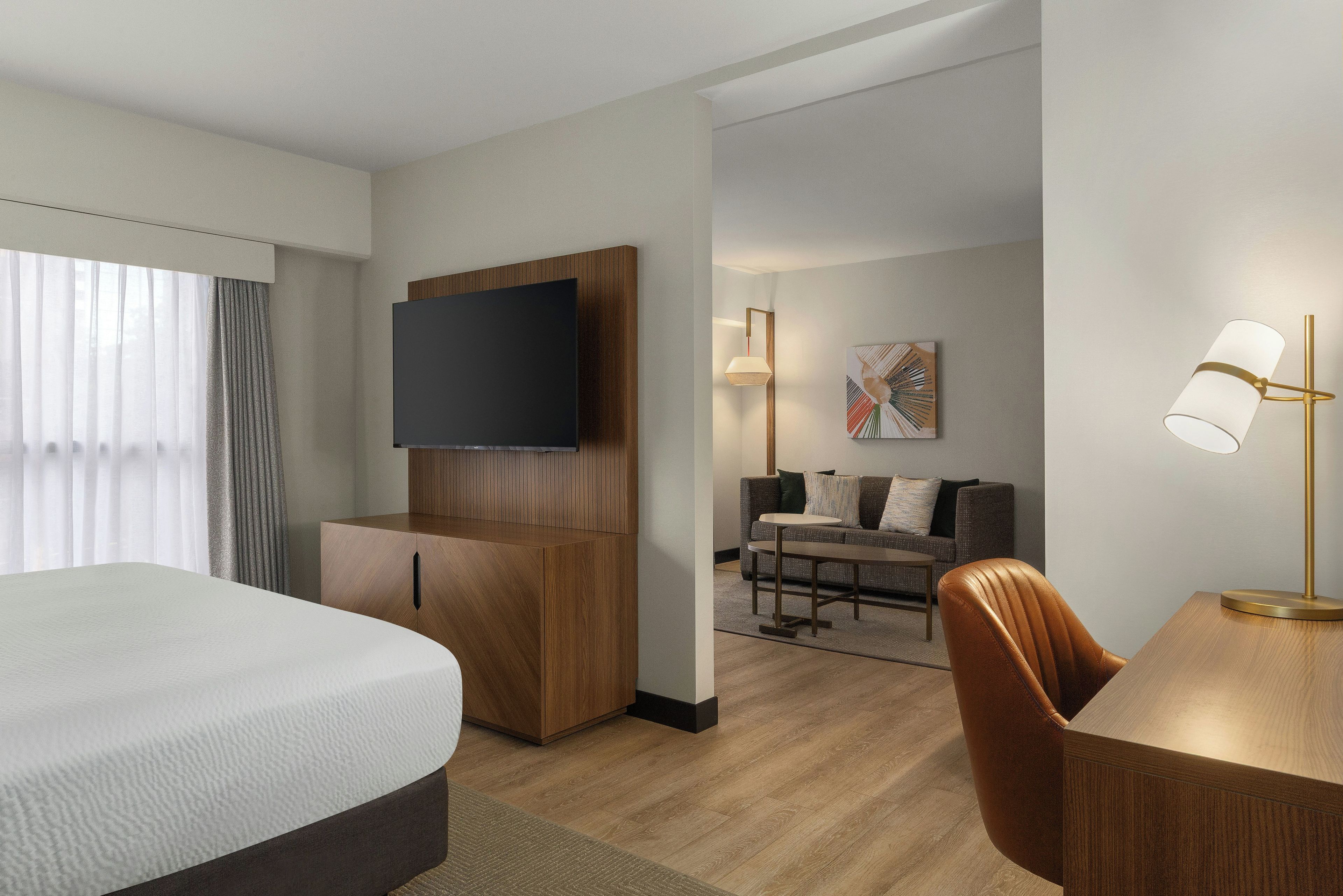 A hotel room with a bed, a TV mounted on a wooden panel, a sofa, a table, and a lamp.