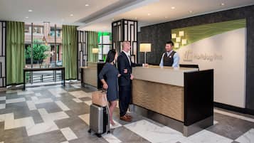 A hotel reception area with a reception desk, a check-in counter, and a view of the outside through large windows.