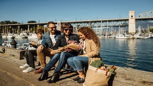 A group of people sitting on a wooden dock by a marina with boats and a bridge in the background. - Holiday Inn & Suites Vancouver Downtown by IHG (Vancouver)