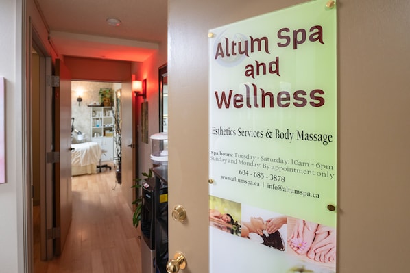 Pasillo que conduce a un cuarto de spa, con un cartel que indica Altum Spa y Bienestar, ofreciendo servicios de estética y masajes corporales.