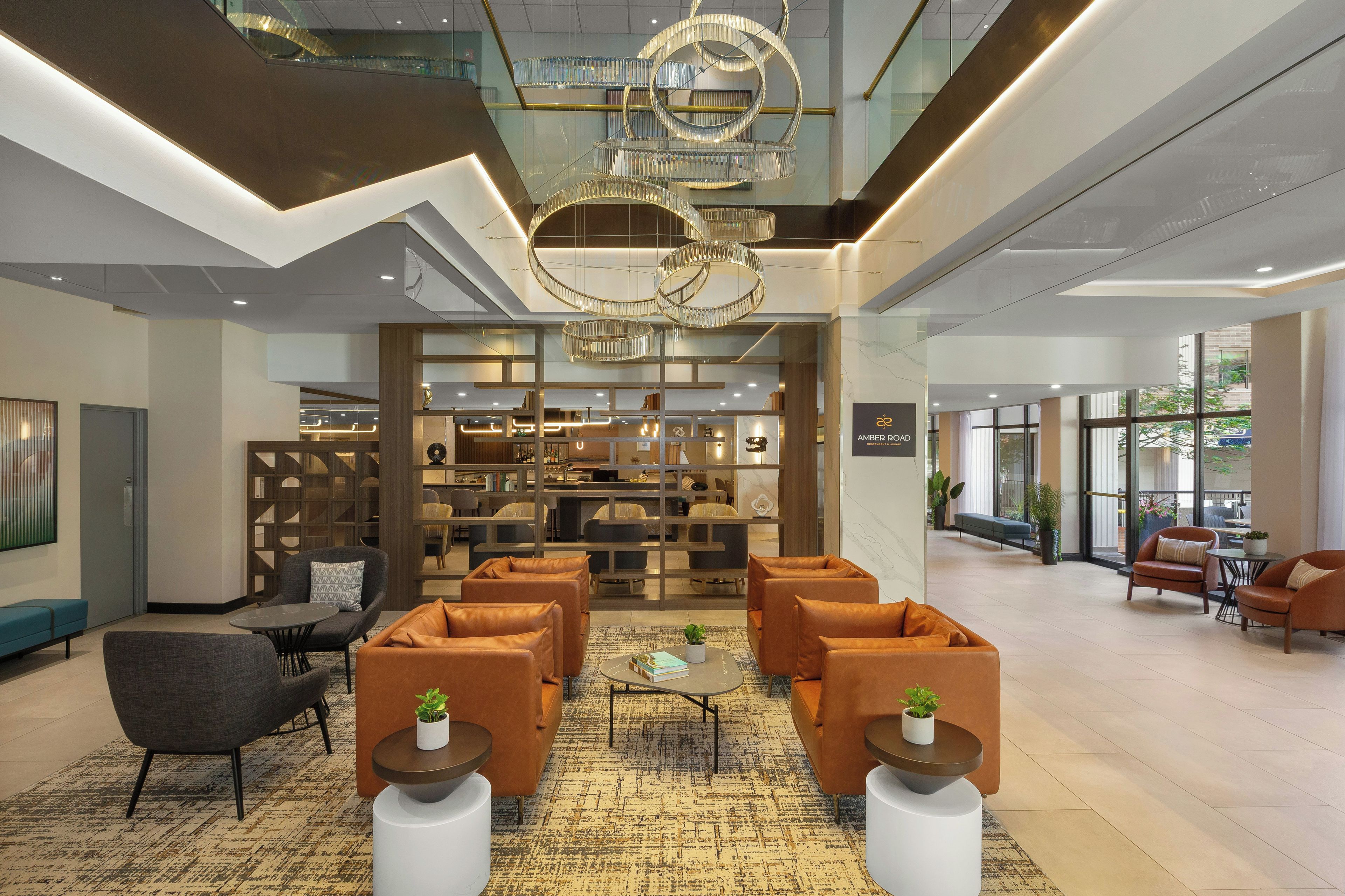 A spacious lobby with a modern chandelier, seating area, and a bar/lounge with a view.
