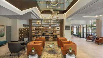 A spacious lobby with a modern chandelier, seating area, and a bar/lounge with a view.
