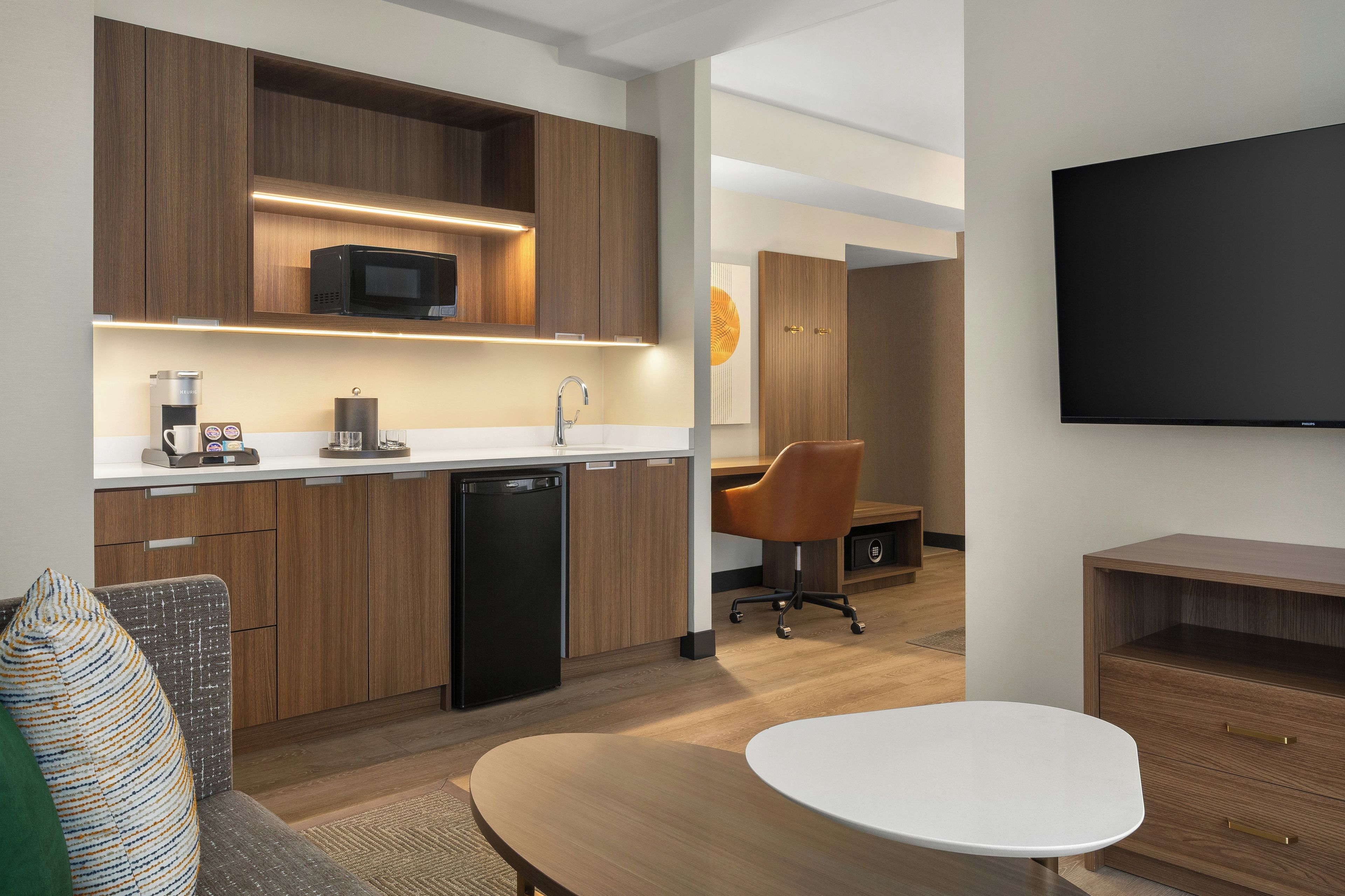 A modern kitchen with built-in appliances, a dining area with a white table, and a flat-screen TV mounted on the wall.