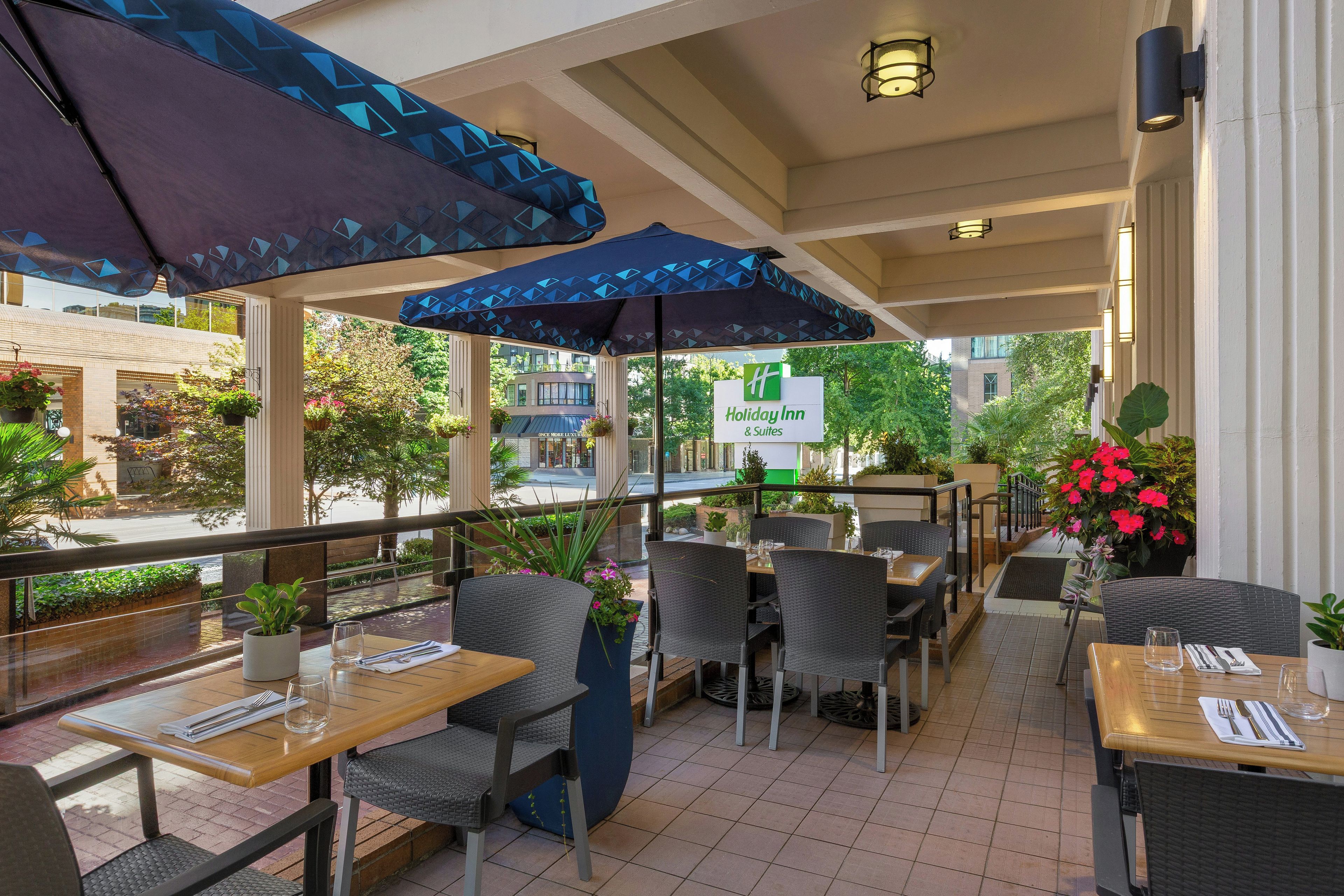 An outdoor seating area with tables and chairs, umbrellas, and a view of the street.