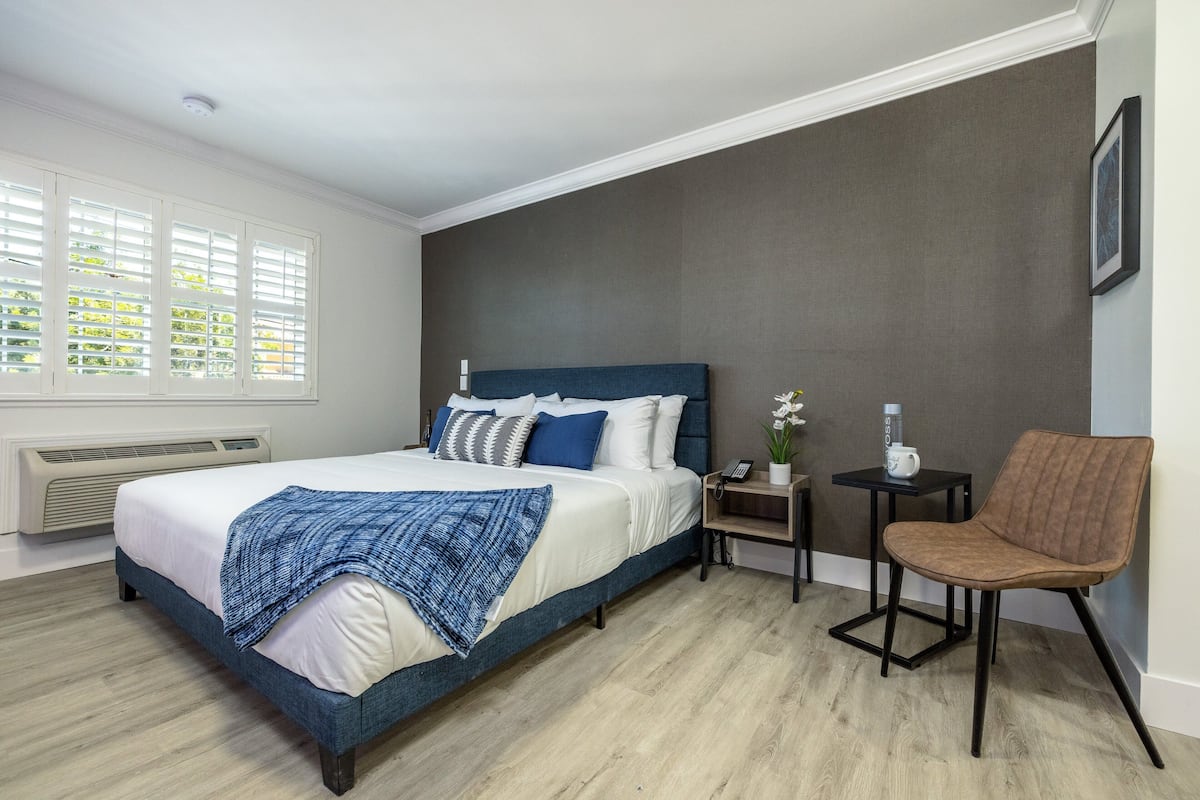 A bedroom with a bed, a chair, a small table, and a heater.
