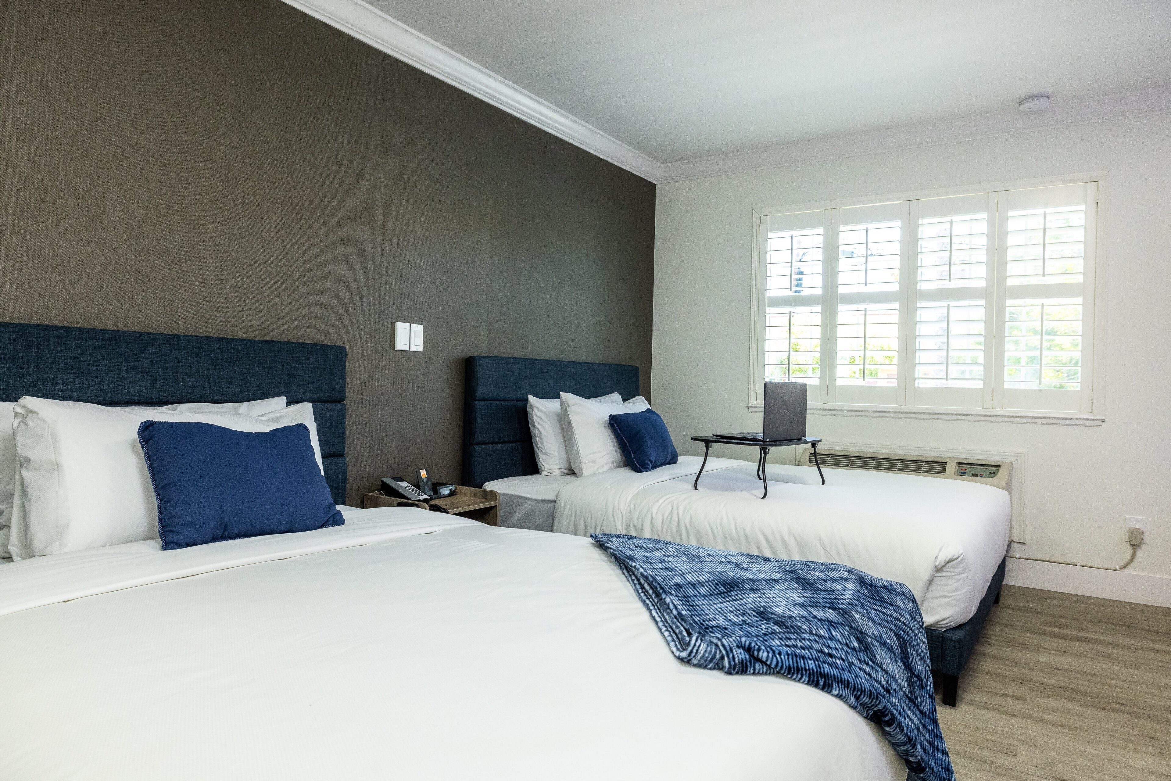Une chambre d’hôtel avec deux lits, un bureau et une fenêtre avec des stores.