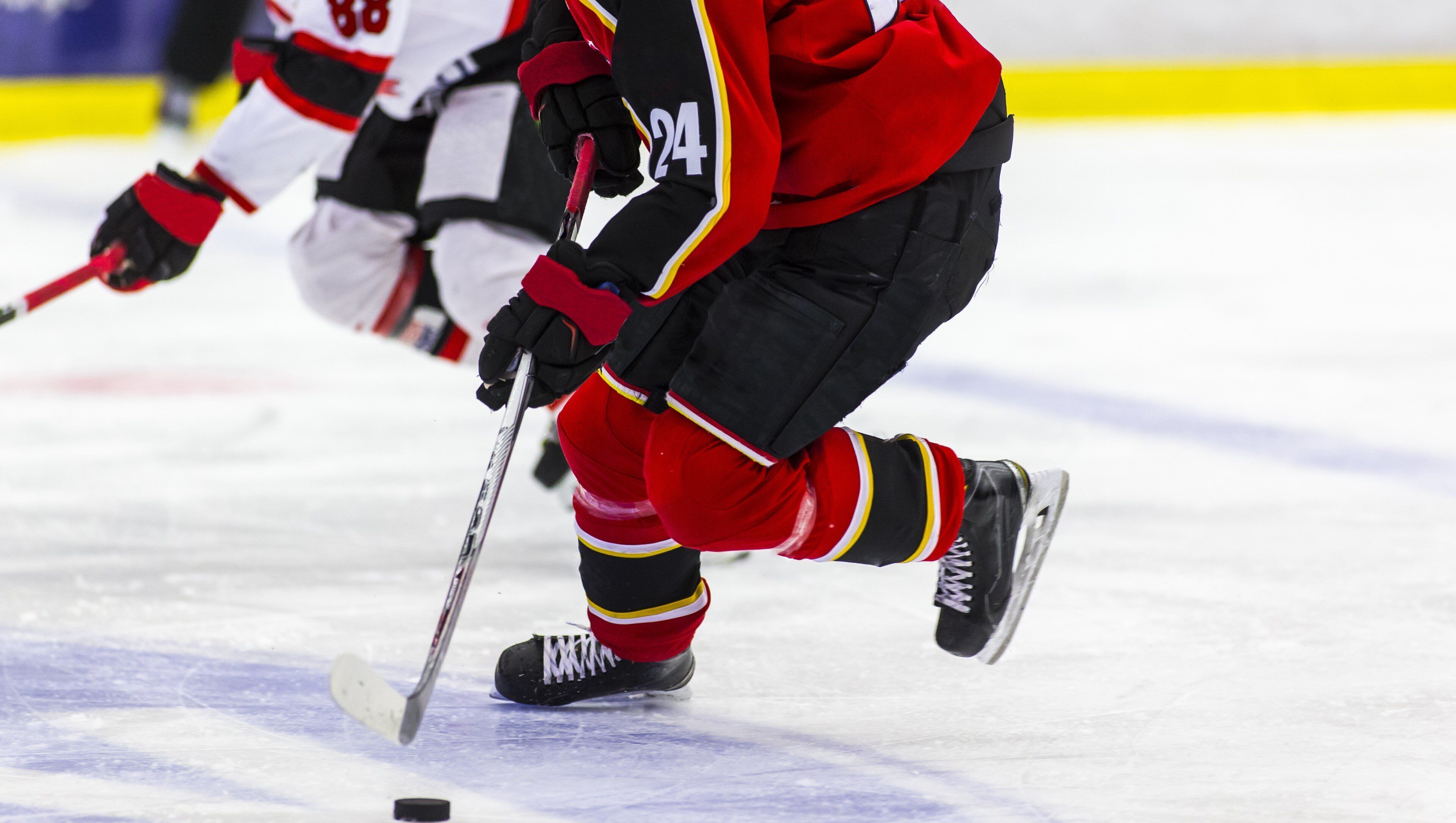 A close-up of an ice hockey player in red and black gear, holding a hockey stick, on the ice.