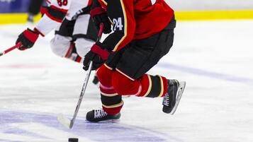 A close-up of an ice hockey player in red and black gear, holding a hockey stick, on the ice.