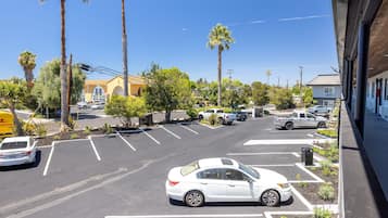 A parking lot with several cars, including a white sedan and a white pickup truck. There are palm trees and a building with a yellow facade in the background.