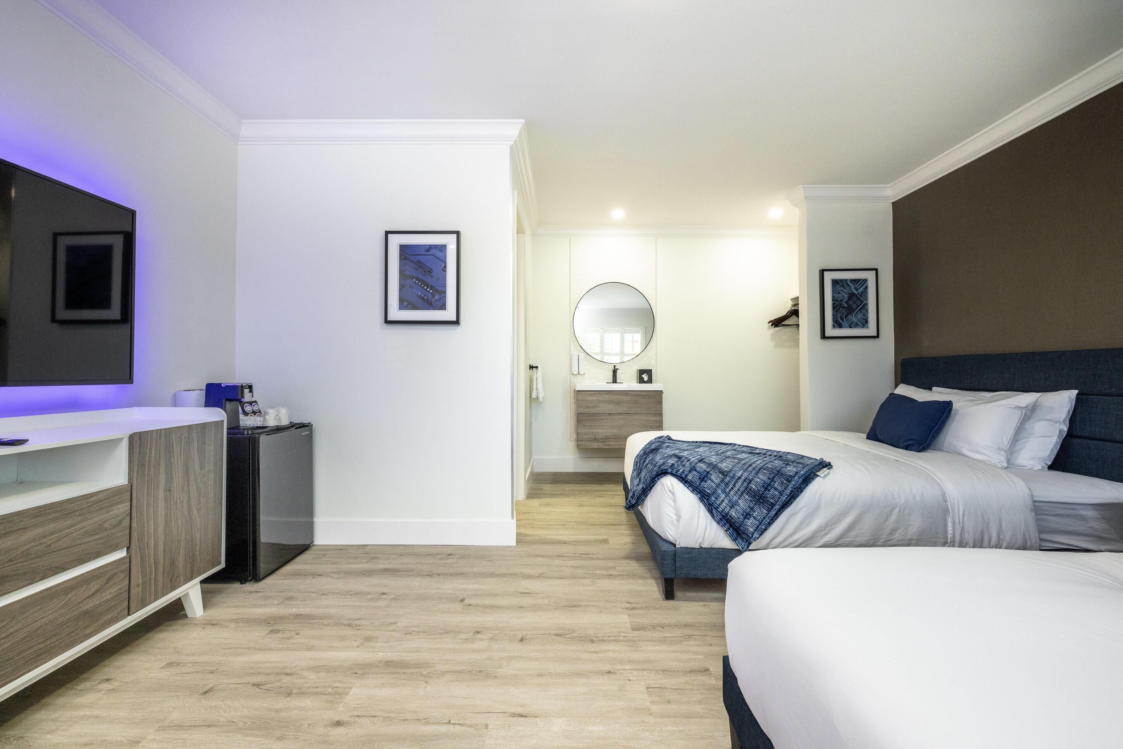 Una habitación de hotel moderna con cama, mesita de noche, espejo y un escritorio pequeño con silla.