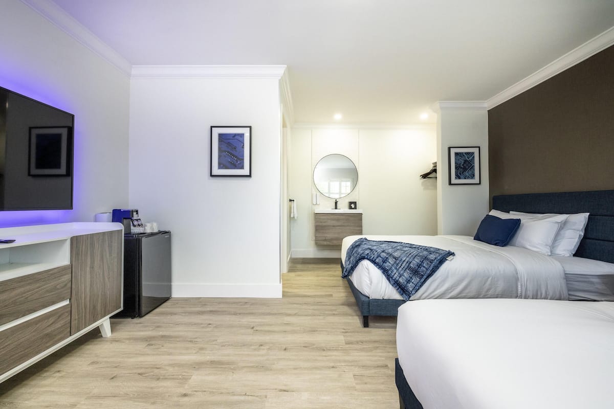 A modern hotel room with a bed, bedside table, mirror, and a small desk with a chair.