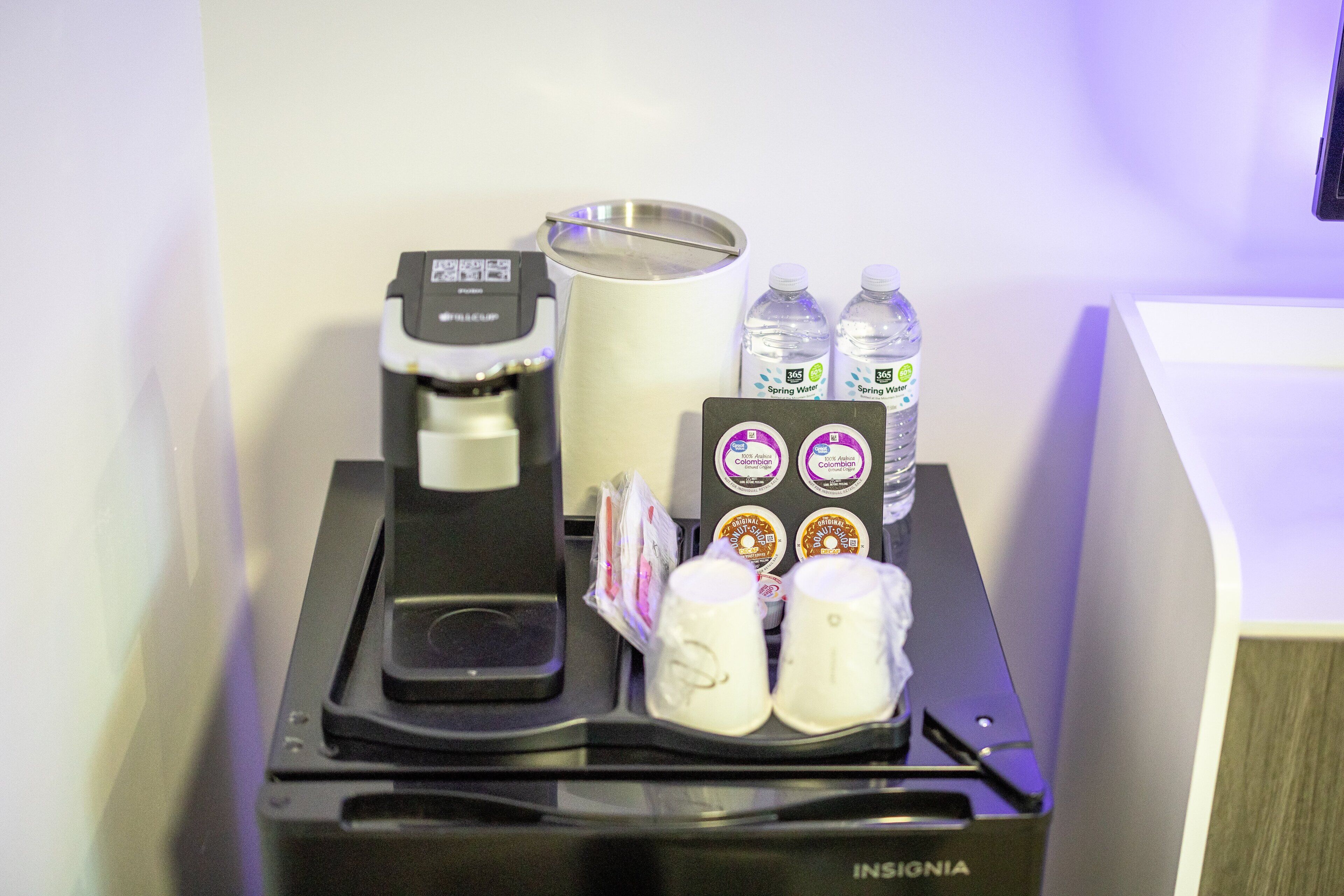 Un espace de libre-service où l'on peut se servir des boissons, avec une machine à café, des bouteilles d'eau et des gobelets jetables.