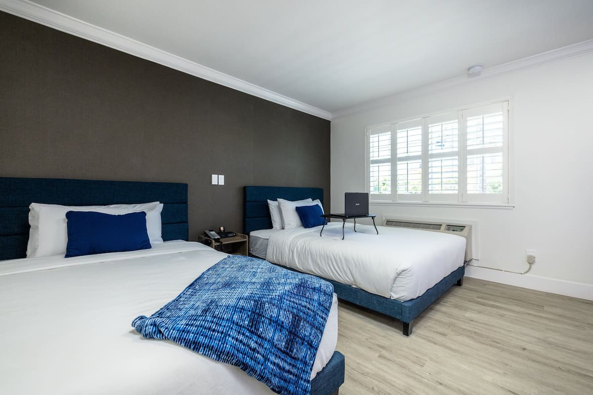 A hotel room with two beds, a large window, and a thermostat on the wall.