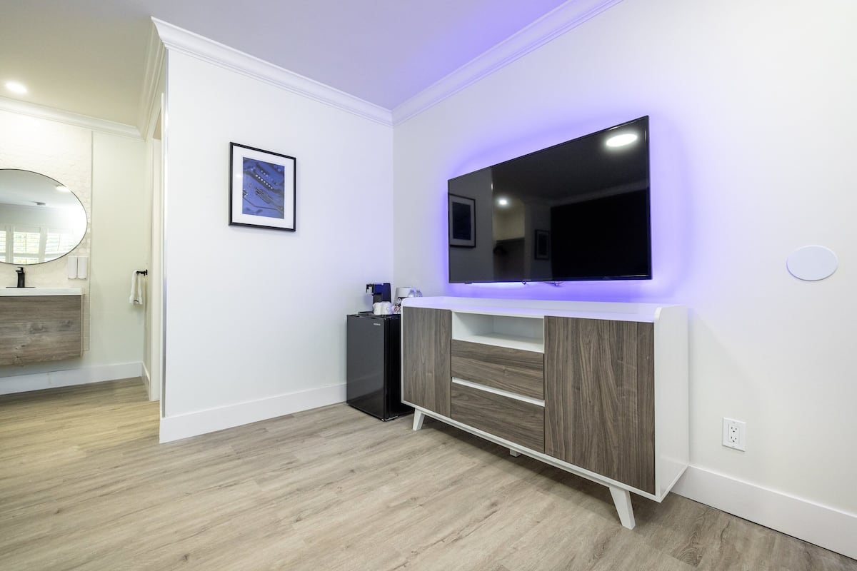 A modern bathroom with a large mirror, a framed picture, and a flat-screen TV mounted on the wall.