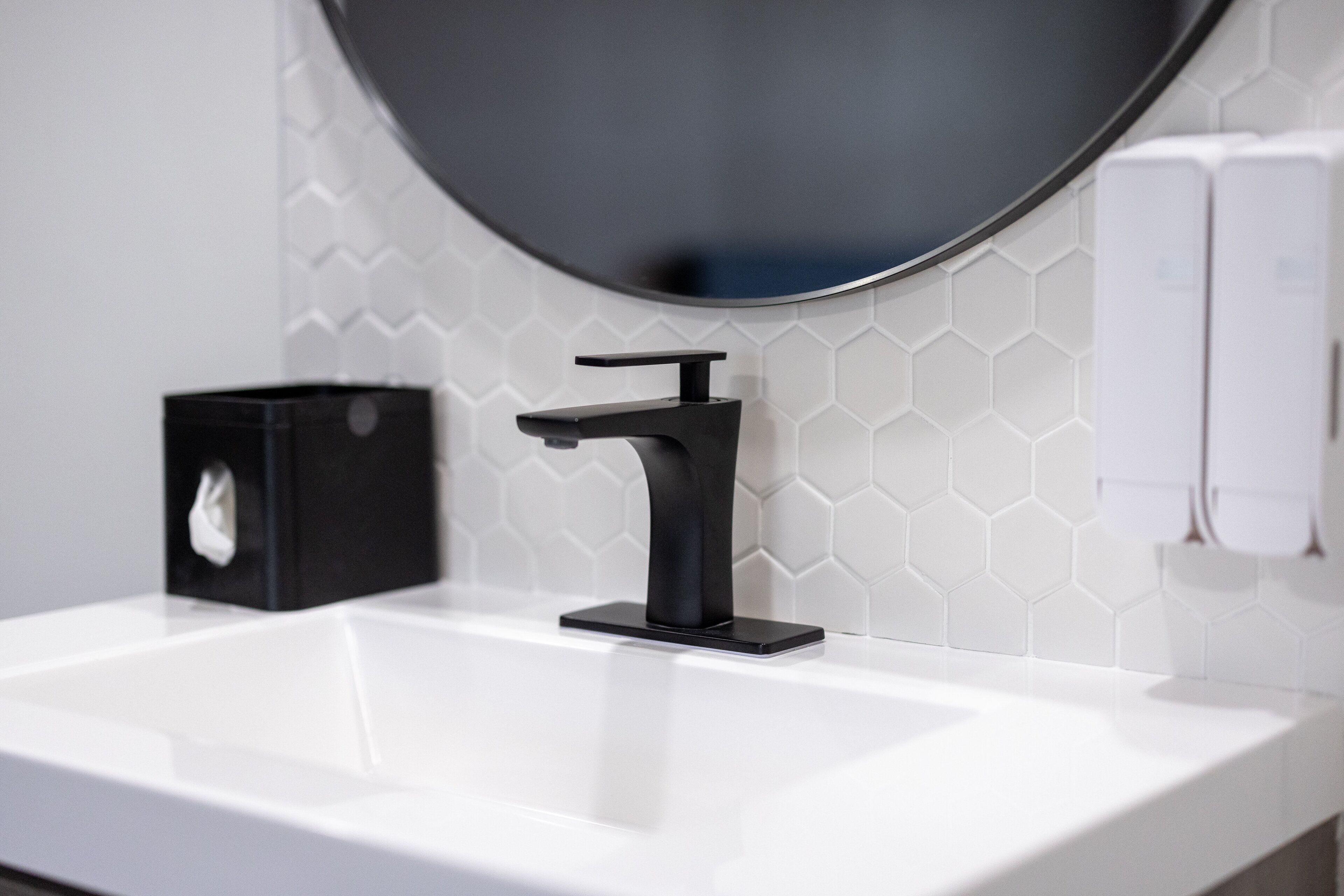 Un baño moderno con un lavabo blanco, grifo negro y dispensador de jabón.