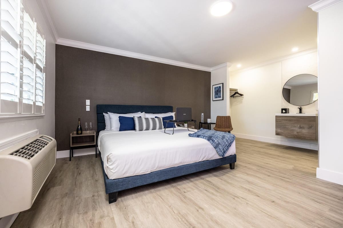A modern hotel room with a large bed, bedside tables, a heater, a mirror, and a view of the city.