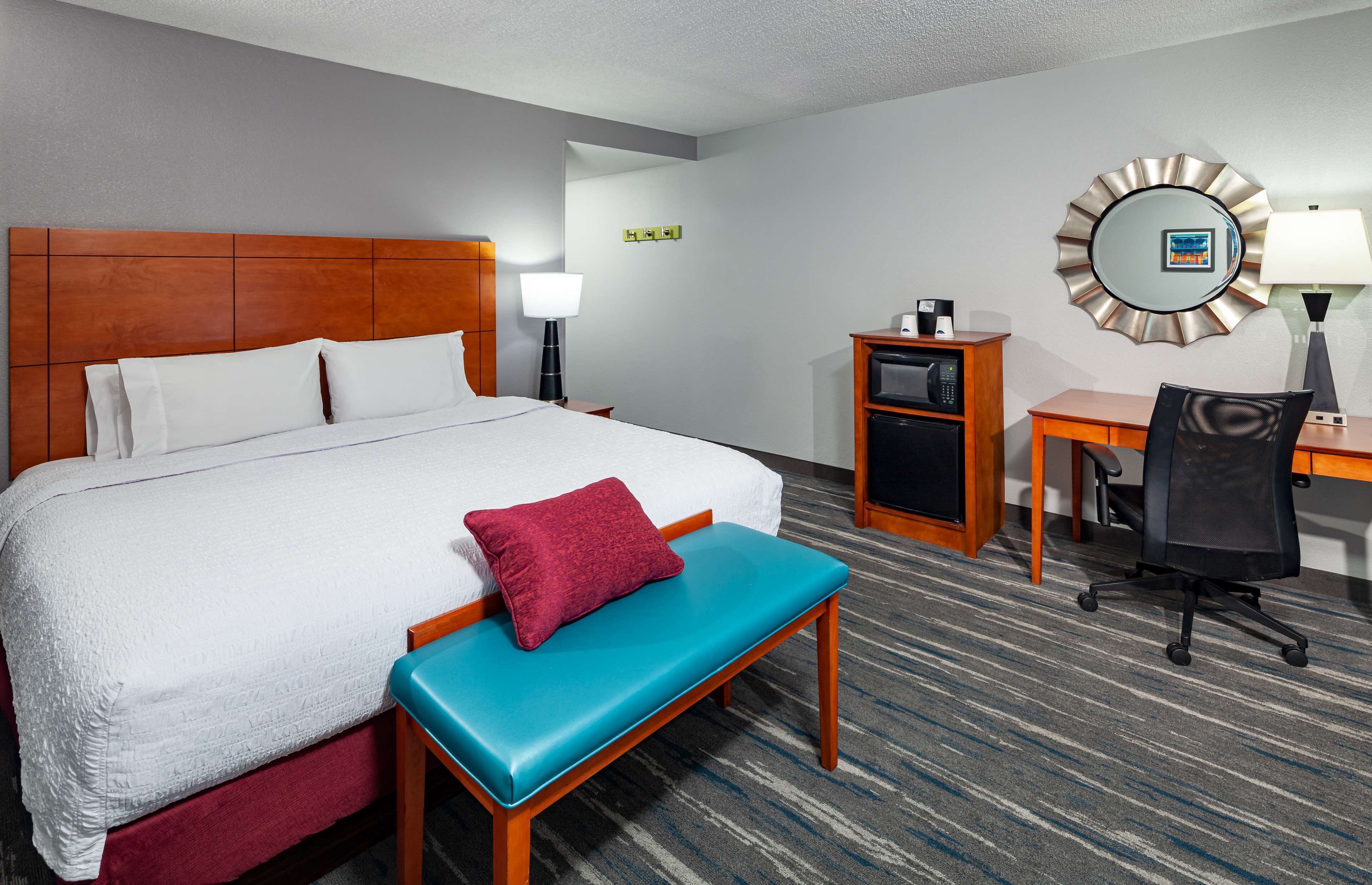 A hotel room with a large bed, a desk, a chair, a small cabinet, and a mirror on the wall.