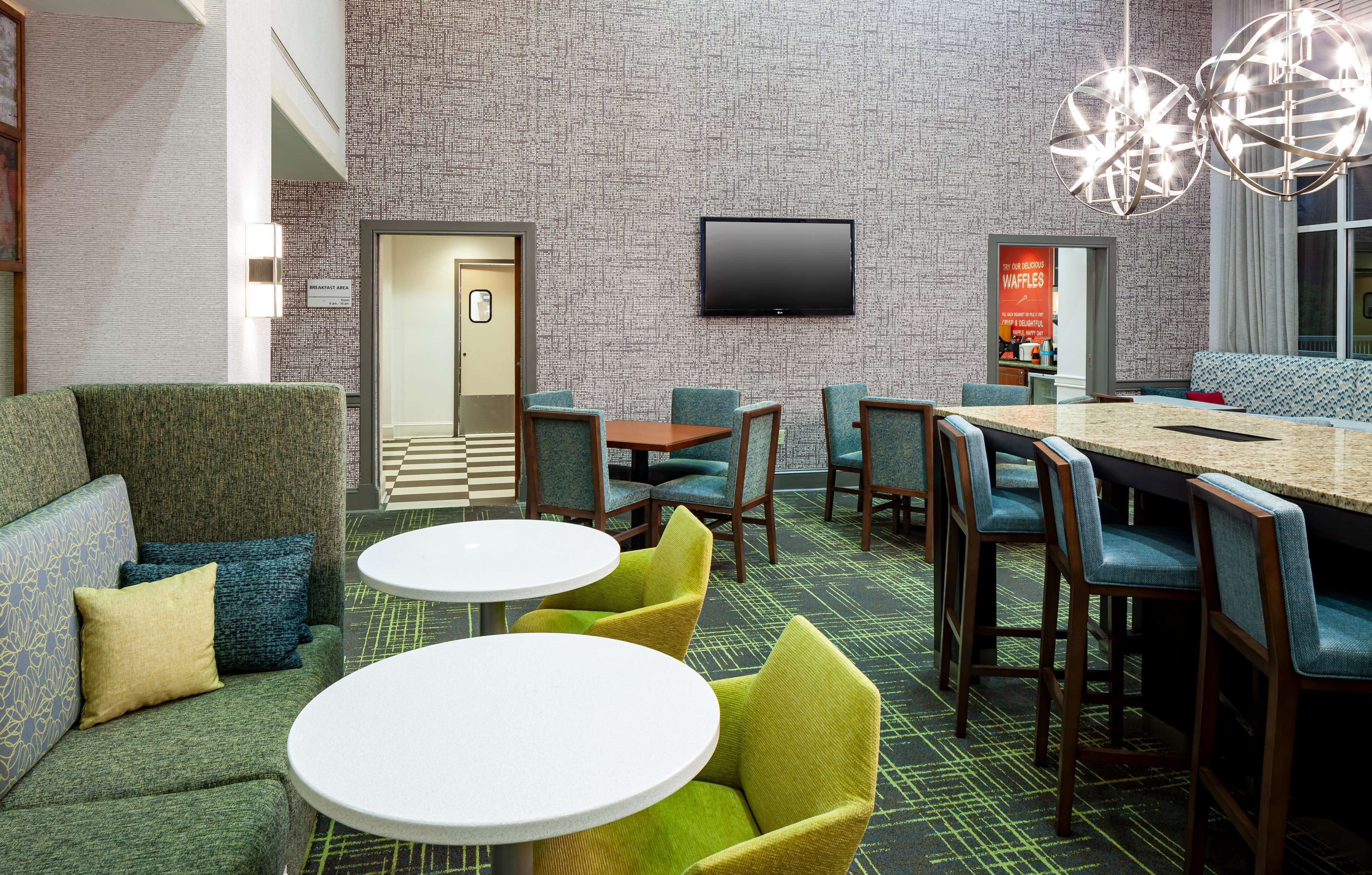Eine Hotelhalle mit strukturierten Wänden, einem Flachbildfernseher, einer Sitzecke mit Sofas und Sesseln sowie einem kleinen Tisch.