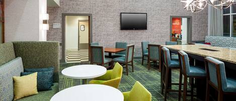 Eine Hotelhalle mit strukturierten Wänden, einem Flachbildfernseher, einer Sitzecke mit Sofas und Sesseln sowie einem kleinen Tisch.
