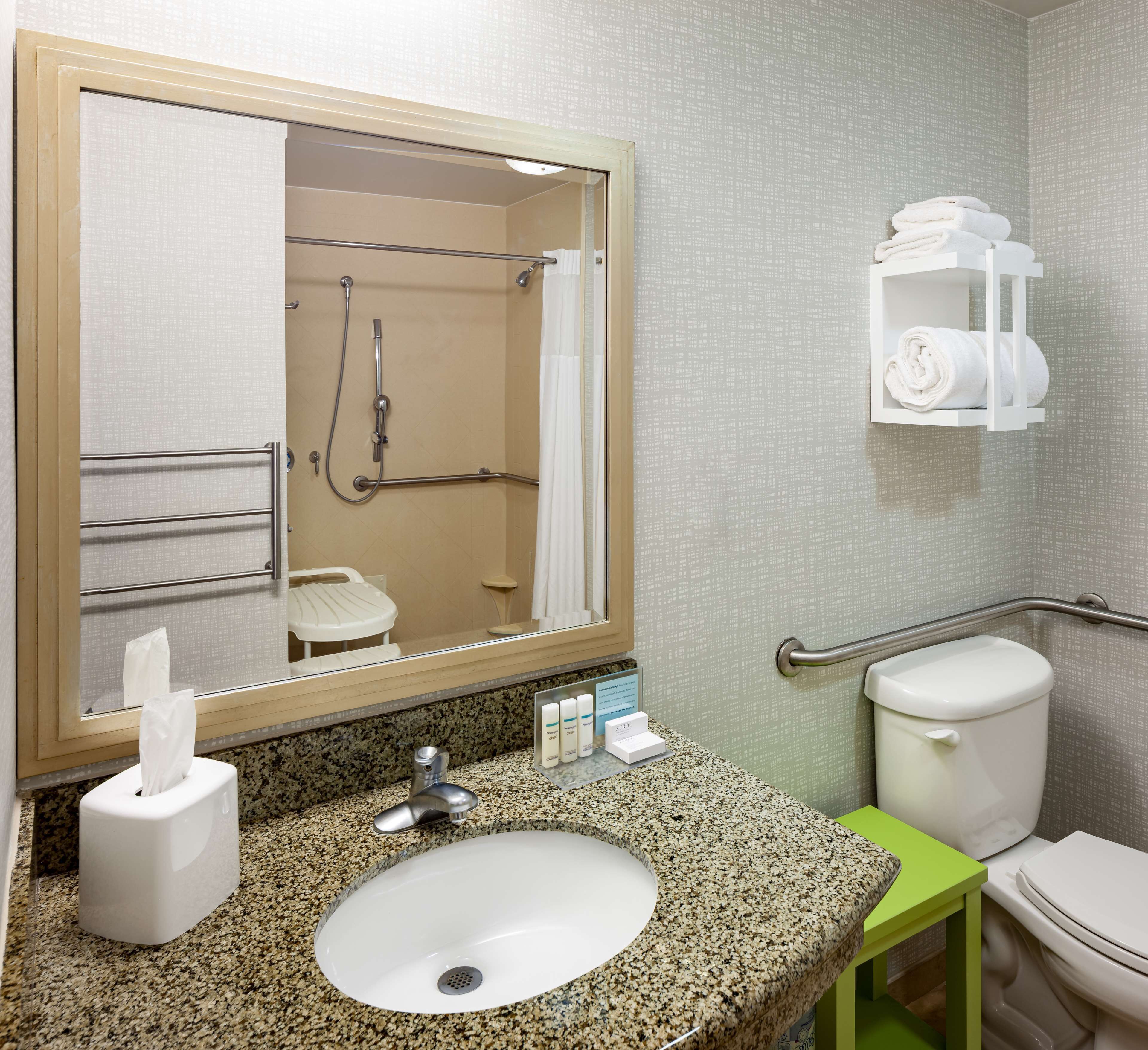 Un baño con encimera de granito, lavamanos blanco, espejo, toallero, inodoro y barra de apoyo.