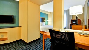 A hotel room with a flat-screen TV, a desk with a lamp, a chair, and a bed with a blue headboard. - Fairfield Inn & Suites Dallas Medical/Market Center (Dallas)