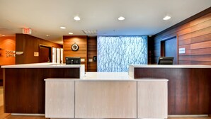A reception area with a wooden reception desk, a clock, and a window with a tree pattern. - Fairfield Inn & Suites Dallas Medical/Market Center (Dallas)