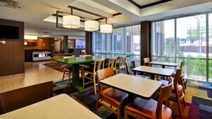 A modern restaurant with a green bar area, wooden tables and chairs, and large windows offering a view of the outdoors. - Fairfield Inn & Suites Dallas Medical/Market Center (Dallas)