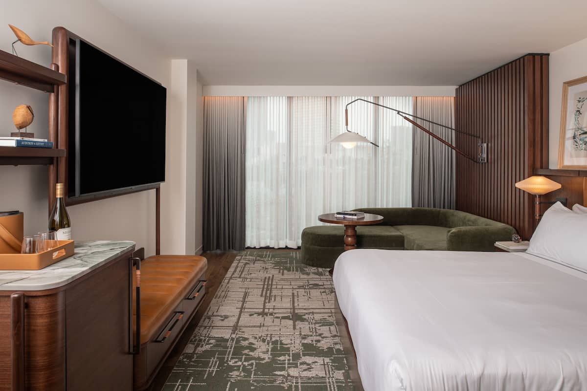 Habitación de hotel con cama, sofá, televisor, escritorio y ventana con cortinas.