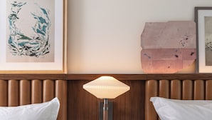A hotel room with two beds, a nightstand with a lamp, a framed artwork, and a decorative wall piece. - The Greenleigh, River Oaks, Autograph Collection (Houston)