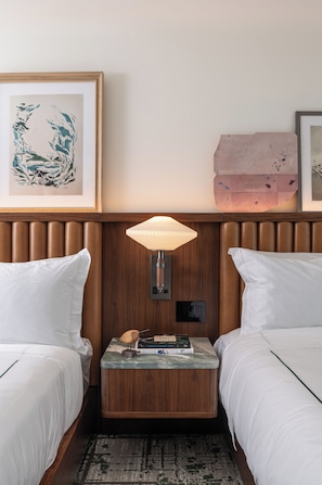 A hotel room with two beds, a nightstand with a lamp, a framed artwork, and a decorative wall piece.