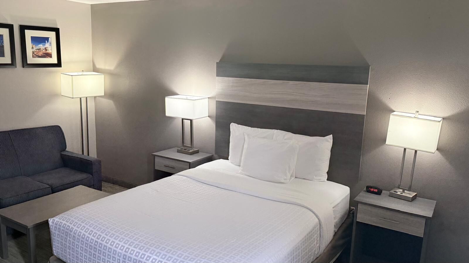 A hotel room with a bed, two bedside tables, a nightstand, a sofa, and two wall-mounted lamps.