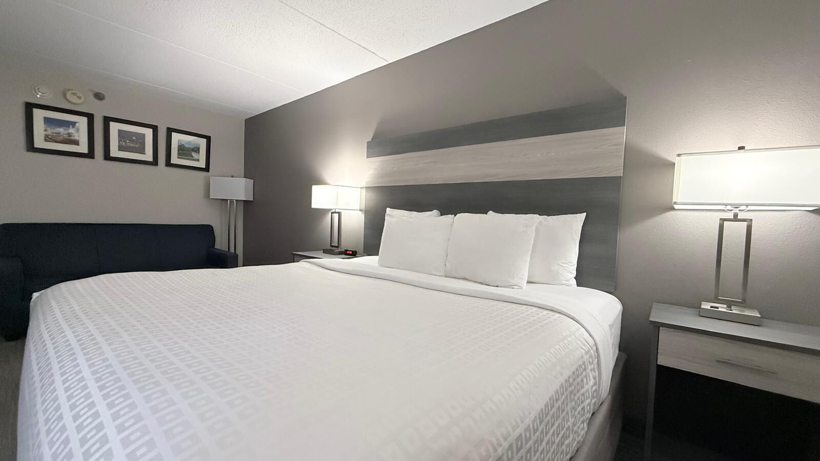 A hotel room with a large bed, two bedside tables with lamps, a dark-colored headboard, and framed pictures on the wall.