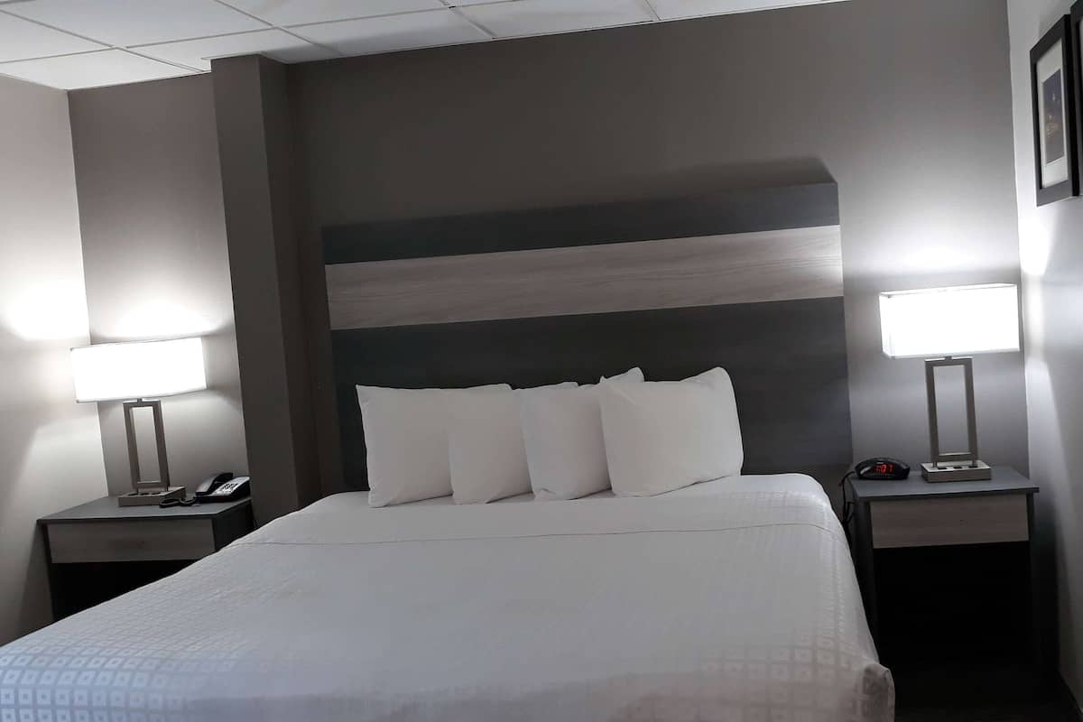 A hotel room with a large bed, two bedside tables, a nightstand, a lamp, a phone, and a clock.