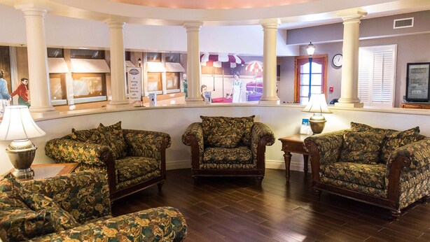 A lobby with a wooden floor, three patterned armchairs, a lamp, and a large window with a view of a building. - Baymont Inn & Suites by Wyndham Lafayette/Purdue Area (Lafayette)