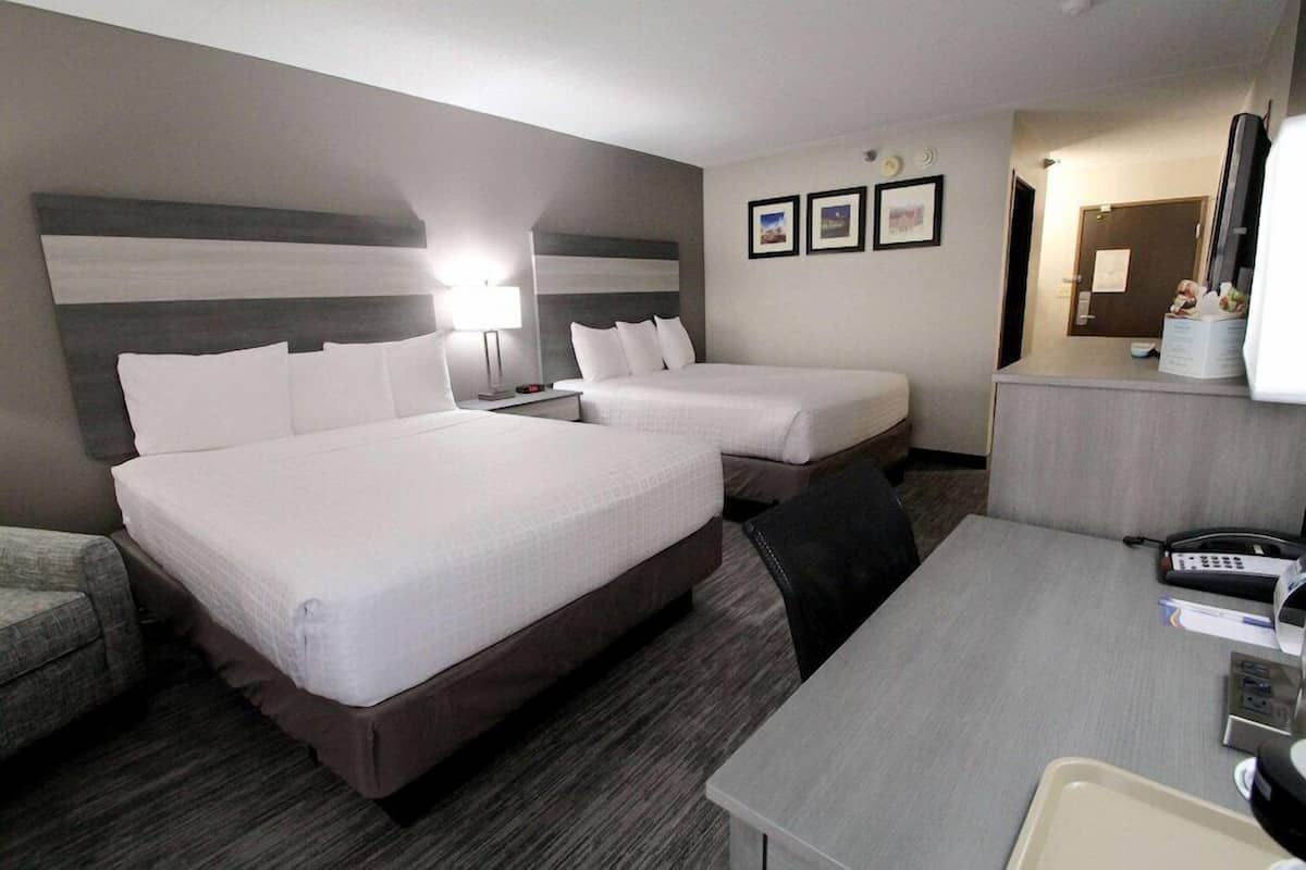 A hotel room with two beds, a desk, a chair, a desk lamp, a phone, and a TV.