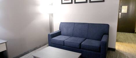 A room with a blue sofa, a small table, and three framed pictures on the wall.