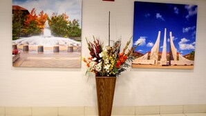 A wall with two framed pictures, one of a fountain and one of a monument, and a wooden planter with flowers in the center. - Baymont Inn & Suites by Wyndham Lafayette/Purdue Area (Lafayette)