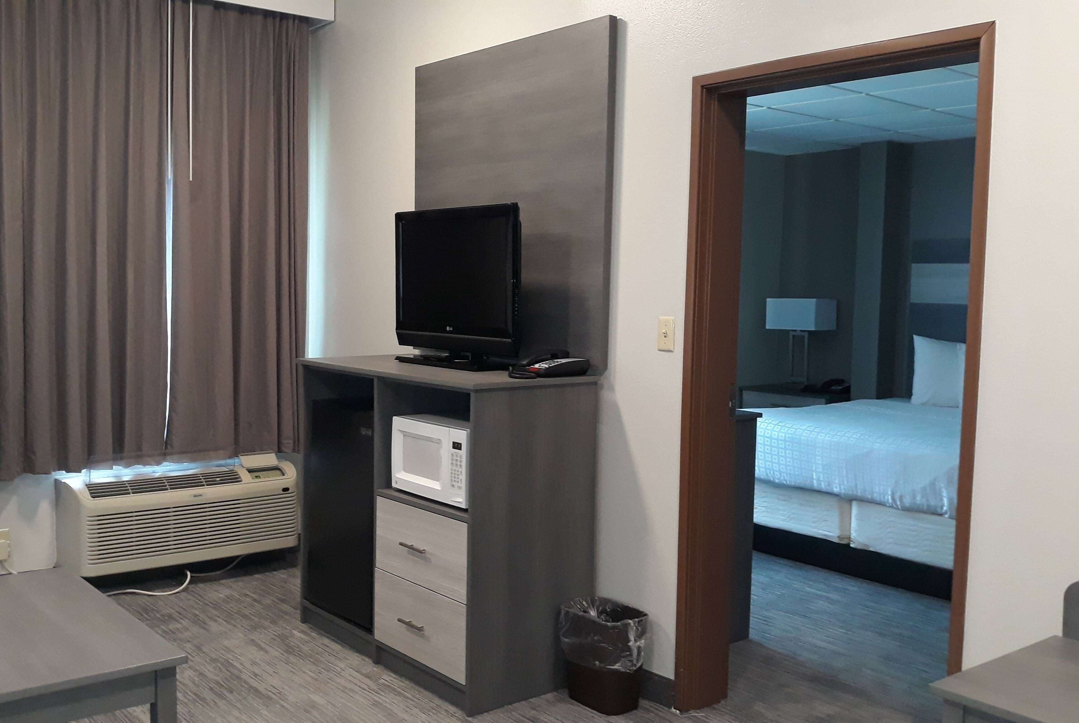 A hotel room with a flat-screen TV on a stand, a microwave, a small trash bin, and a bed with white bedding.